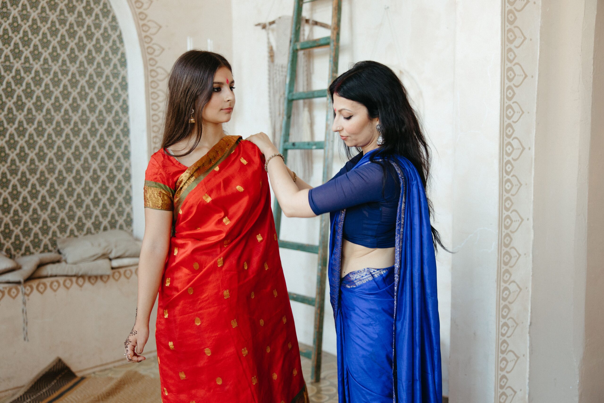 Two South Asian women wearing traditional sarees and preparing indoors.